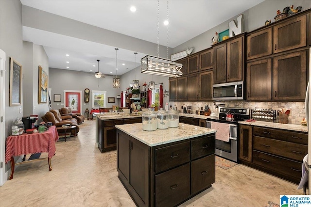 kitchen featuring decorative backsplash, dark brown cabinetry, a kitchen island, ceiling fan, and appliances with stainless steel finishes