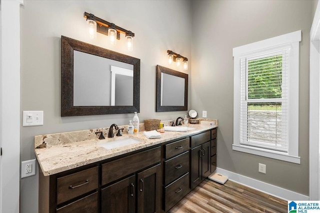 full bath with a sink, baseboards, double vanity, and wood finished floors