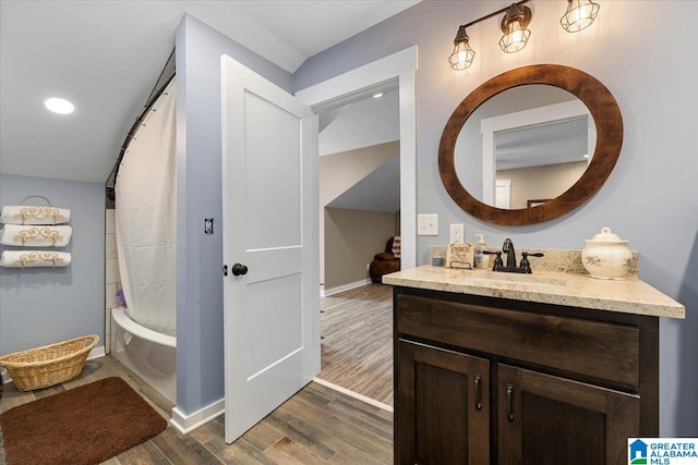 bathroom featuring shower / bath combination with curtain, wood finished floors, vanity, baseboards, and recessed lighting
