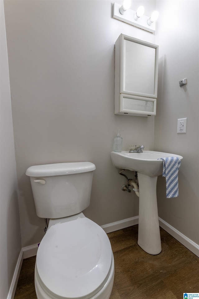 half bathroom with baseboards, toilet, and wood finished floors