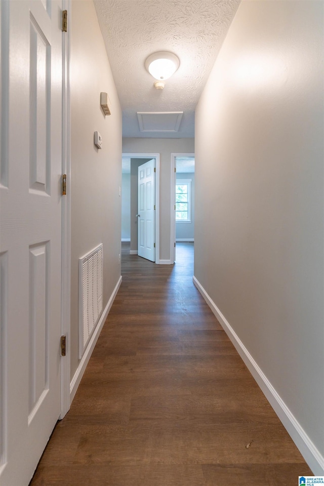 corridor featuring baseboards, attic access, a textured ceiling, and visible vents