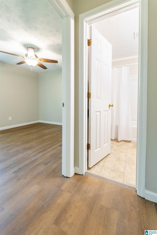 hallway featuring a textured ceiling, baseboards, and wood finished floors