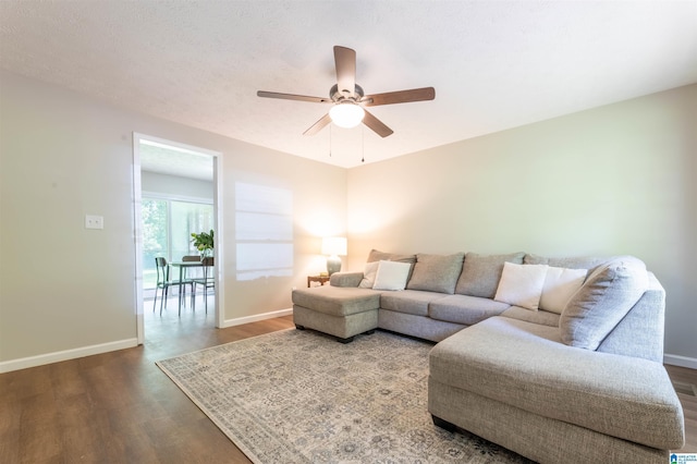 living room featuring ceiling fan, baseboards, and dark wood-type flooring