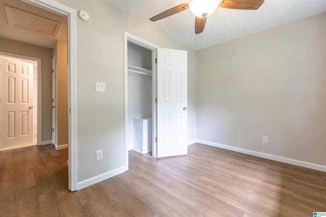unfurnished bedroom with baseboards, attic access, wood finished floors, and a closet