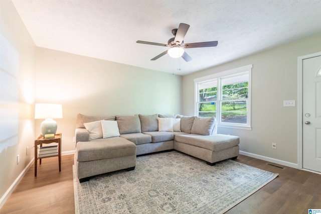 living room featuring visible vents, a ceiling fan, baseboards, and wood finished floors