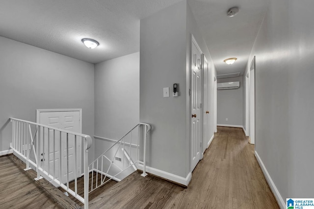 hall with baseboards, a wall mounted AC, wood finished floors, and an upstairs landing