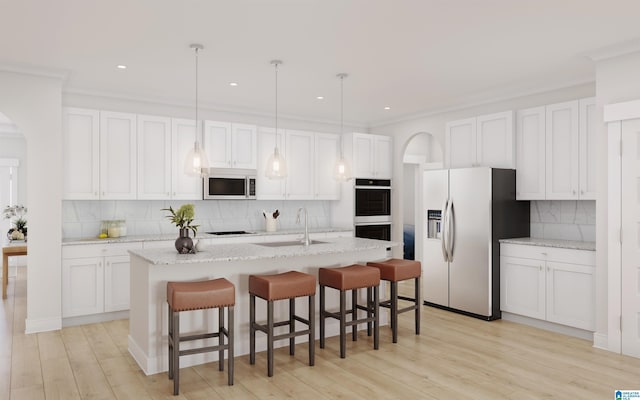 kitchen with white cabinets, appliances with stainless steel finishes, a sink, arched walkways, and backsplash