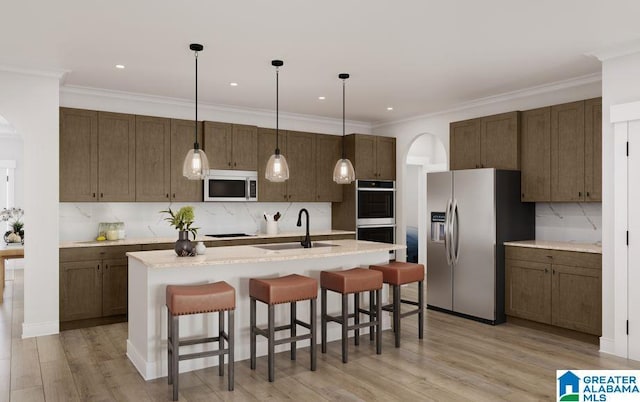 kitchen featuring appliances with stainless steel finishes, a sink, a breakfast bar area, arched walkways, and decorative backsplash
