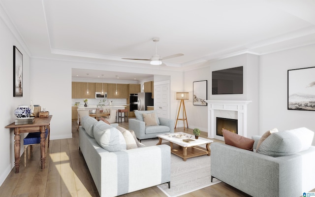 living area featuring light wood-style floors, baseboards, a high end fireplace, a raised ceiling, and a ceiling fan