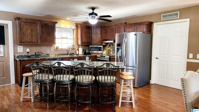 kitchen with light wood-style floors, a sink, appliances with stainless steel finishes, and under cabinet range hood