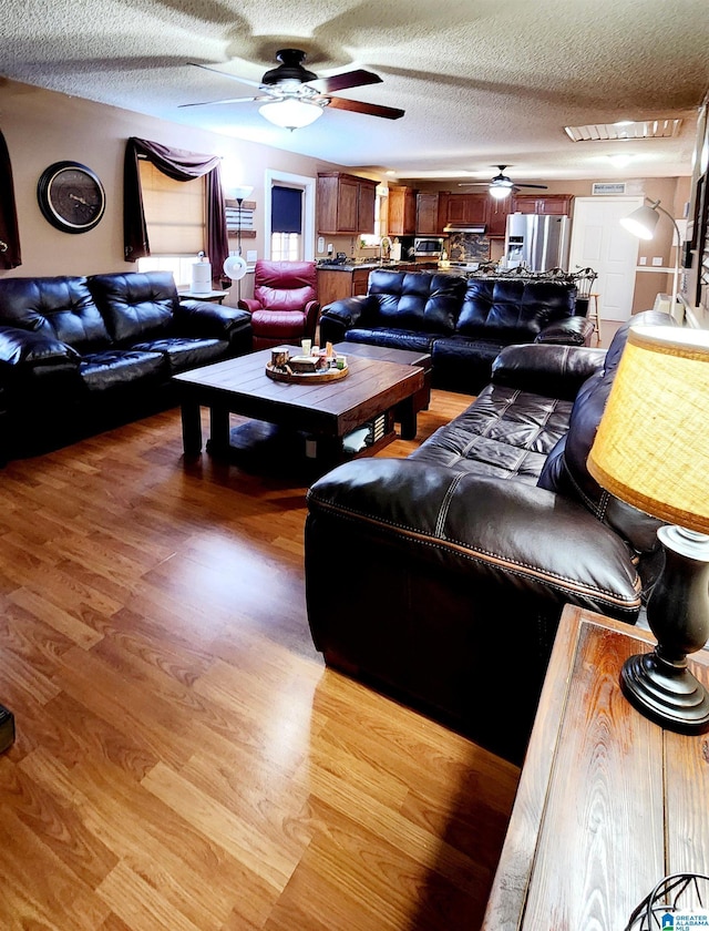 living room featuring a ceiling fan, a textured ceiling, and light wood-type flooring