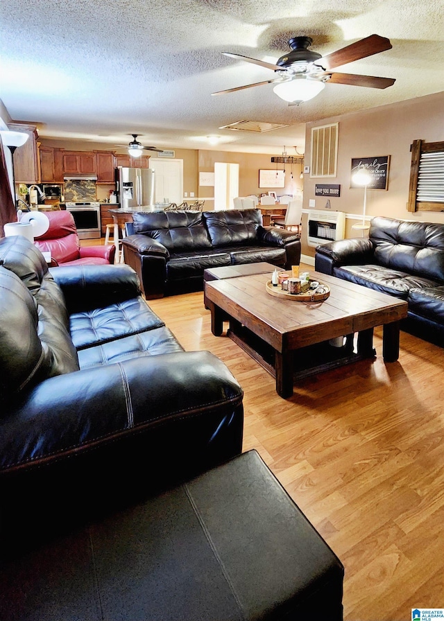 living area with light wood-style floors, a ceiling fan, a textured ceiling, and visible vents