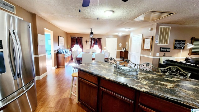 kitchen featuring light wood-style floors, stainless steel fridge with ice dispenser, ceiling fan, and a textured ceiling