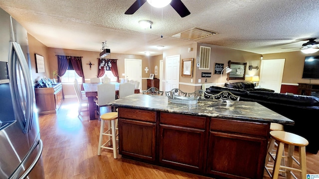 kitchen with ceiling fan, freestanding refrigerator, a textured ceiling, and a kitchen breakfast bar