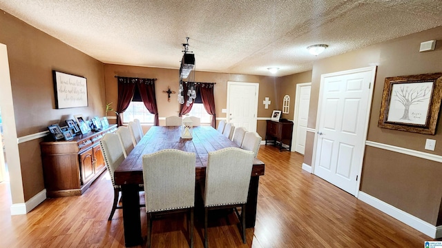 dining space featuring light wood-type flooring, a textured ceiling, and baseboards