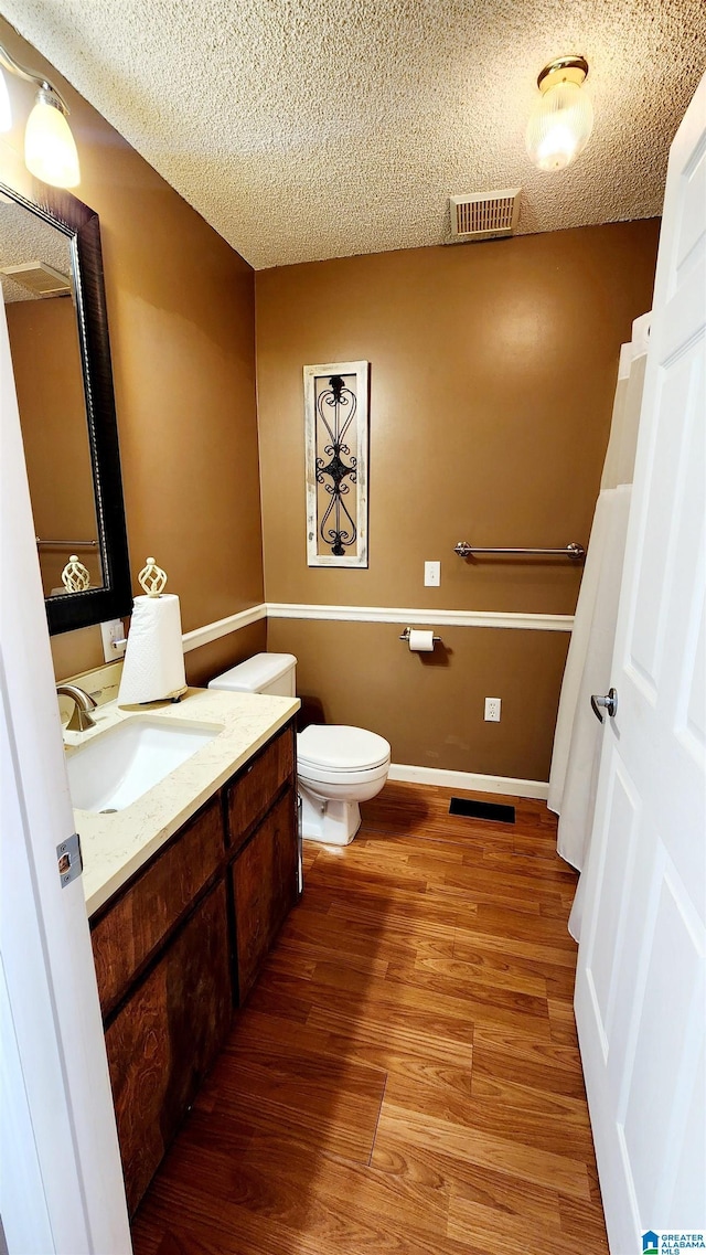 half bathroom with visible vents, vanity, wood finished floors, toilet, and a textured ceiling