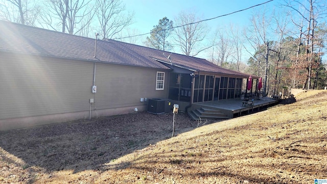 view of side of home with central AC unit, a shingled roof, a sunroom, and a deck