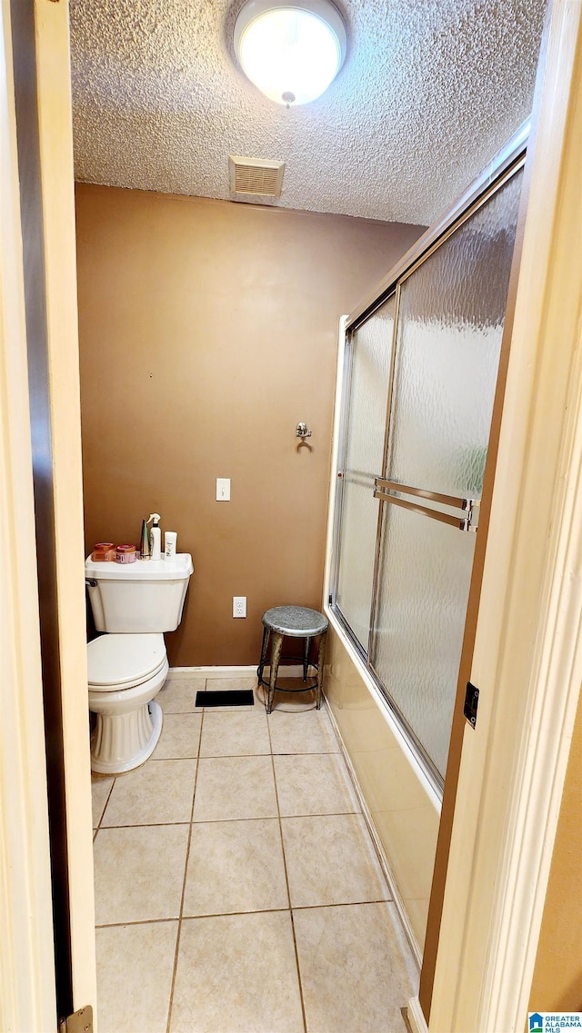 full bath with visible vents, tile patterned flooring, shower / bath combination with glass door, toilet, and a textured ceiling
