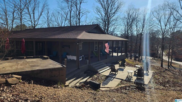 view of property exterior with roof with shingles, covered porch, and a patio area