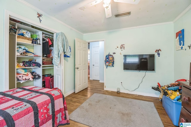 bedroom with visible vents, crown molding, a closet, wood finished floors, and baseboards