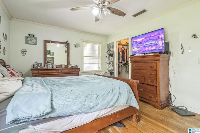 bedroom with a walk in closet, visible vents, wood finished floors, a closet, and ornamental molding