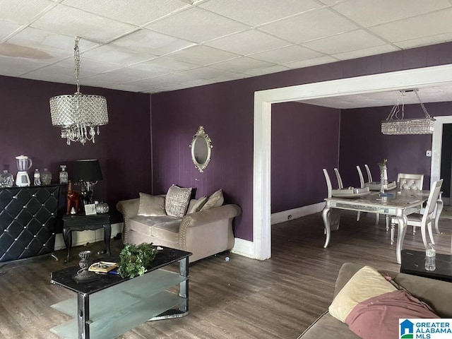 living area featuring baseboards, a paneled ceiling, wood finished floors, and a notable chandelier