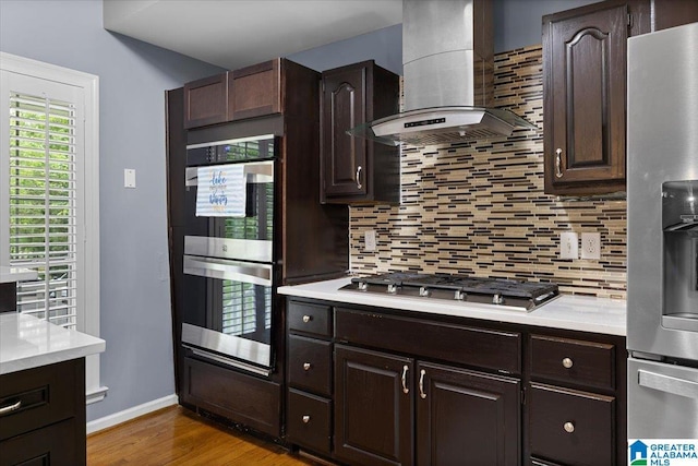 kitchen with light countertops, appliances with stainless steel finishes, decorative backsplash, and wall chimney exhaust hood