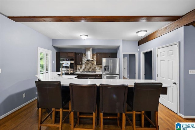 kitchen featuring dark brown cabinetry, beam ceiling, wall chimney range hood, stainless steel refrigerator with ice dispenser, and light countertops