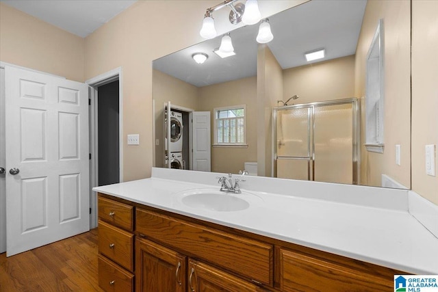 full bath featuring vanity, toilet, stacked washing maching and dryer, wood finished floors, and a stall shower