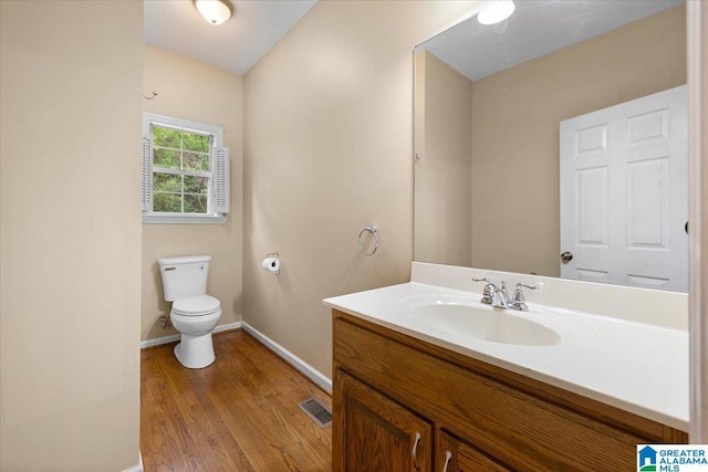 half bathroom featuring vanity, toilet, baseboards, wood finished floors, and visible vents