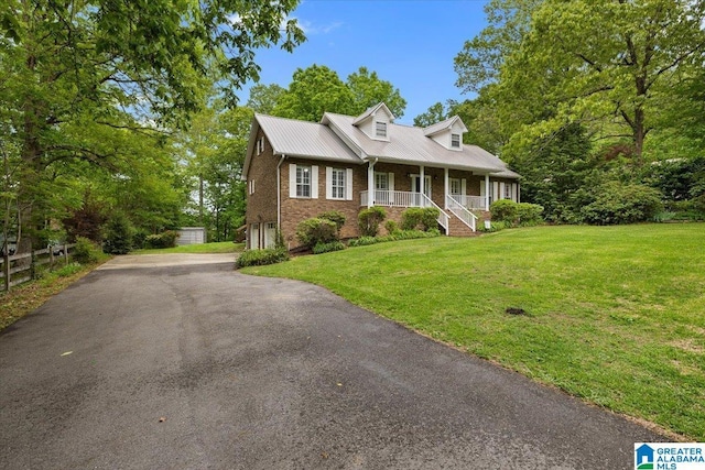 new england style home featuring a front lawn, brick siding, a garage, a porch, and metal roof