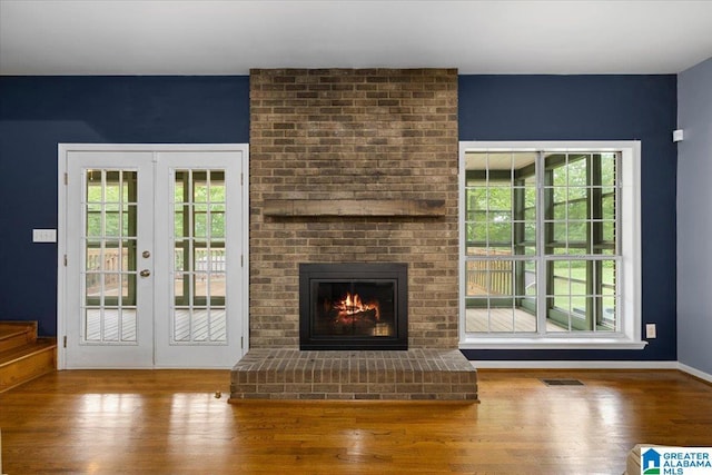 unfurnished living room with a healthy amount of sunlight, a fireplace, french doors, and wood finished floors