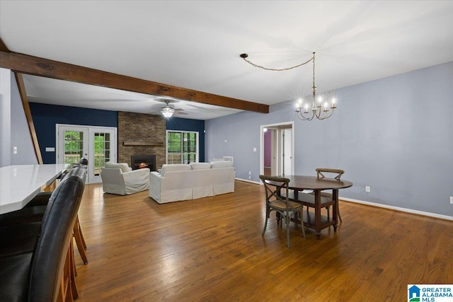 dining room featuring french doors, a fireplace, beam ceiling, wood finished floors, and ceiling fan with notable chandelier
