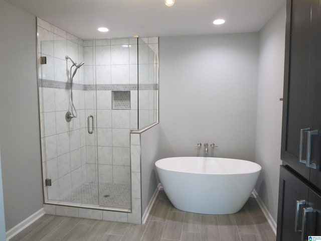 full bath featuring a freestanding bath, a stall shower, wood finish floors, baseboards, and recessed lighting