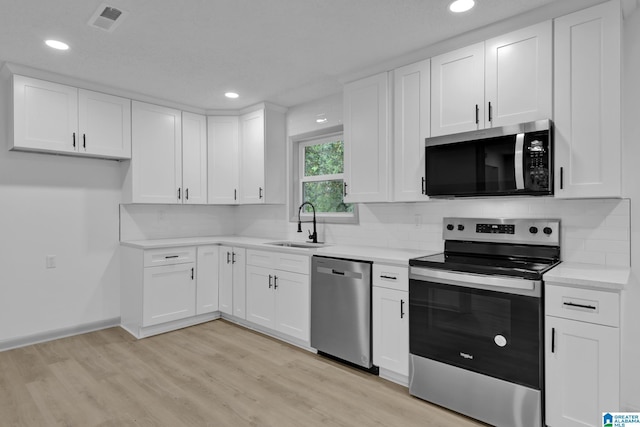 kitchen with visible vents, a sink, white cabinets, stainless steel appliances, and light wood-style flooring