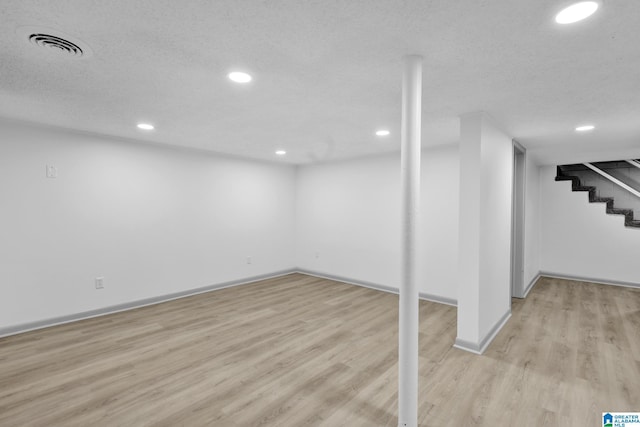 finished below grade area with recessed lighting, baseboards, light wood-style flooring, and stairway