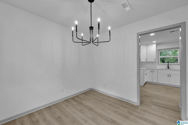 unfurnished dining area with visible vents, a sink, baseboards, a chandelier, and light wood-style flooring