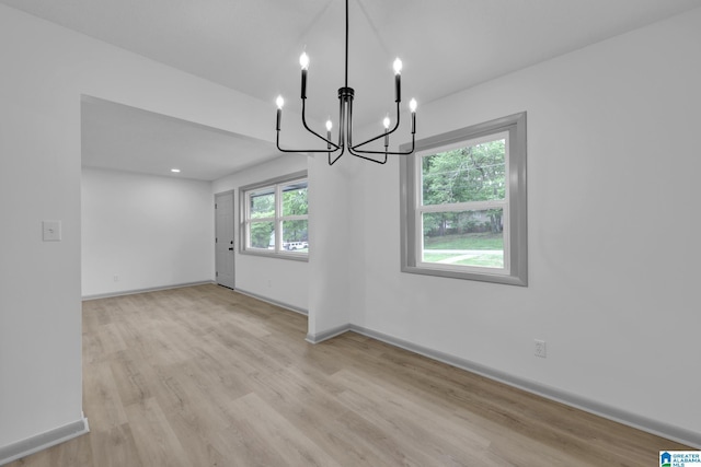 unfurnished dining area featuring baseboards, a notable chandelier, and light wood-type flooring