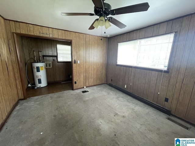 carpeted empty room featuring water heater, ceiling fan, wood walls, and visible vents