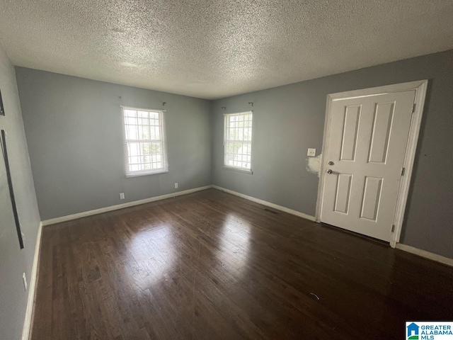 empty room with baseboards, a textured ceiling, wood finished floors, and visible vents
