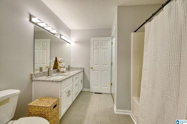 full bath featuring a sink, double vanity, toilet, a textured ceiling, and baseboards