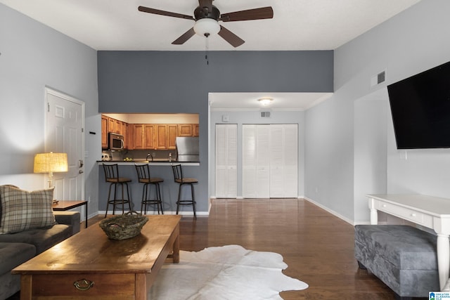 living room with ceiling fan, baseboards, wood finished floors, a towering ceiling, and visible vents