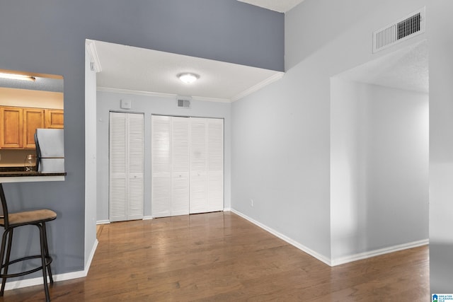 unfurnished bedroom with visible vents, wood finished floors, baseboards, freestanding refrigerator, and ornamental molding