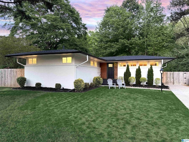 view of front of house with fence, a lawn, and brick siding