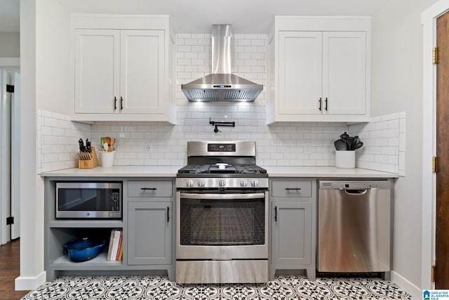 kitchen with light countertops, gray cabinets, stainless steel appliances, and wall chimney exhaust hood