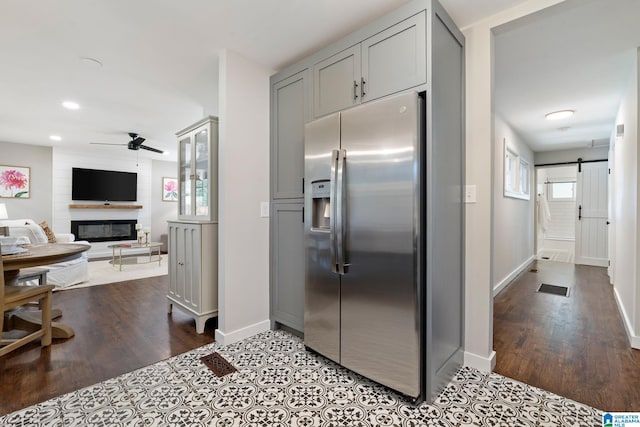 kitchen with gray cabinets, ceiling fan, stainless steel refrigerator with ice dispenser, a fireplace, and baseboards