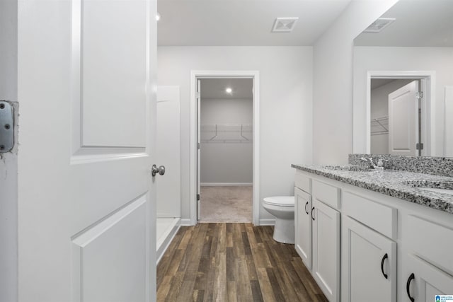 full bath featuring toilet, a spacious closet, wood finished floors, and visible vents