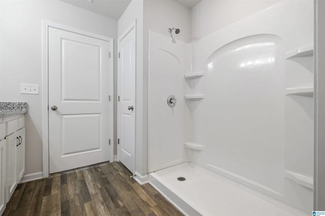 bathroom featuring wood finished floors, baseboards, a shower, and vanity