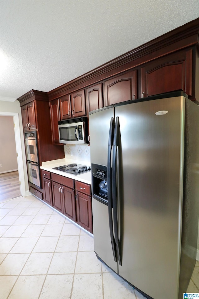 kitchen featuring light countertops, stainless steel appliances, a textured ceiling, and reddish brown cabinets
