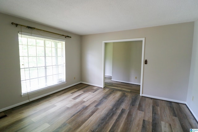 empty room with baseboards, plenty of natural light, a textured ceiling, and wood finished floors